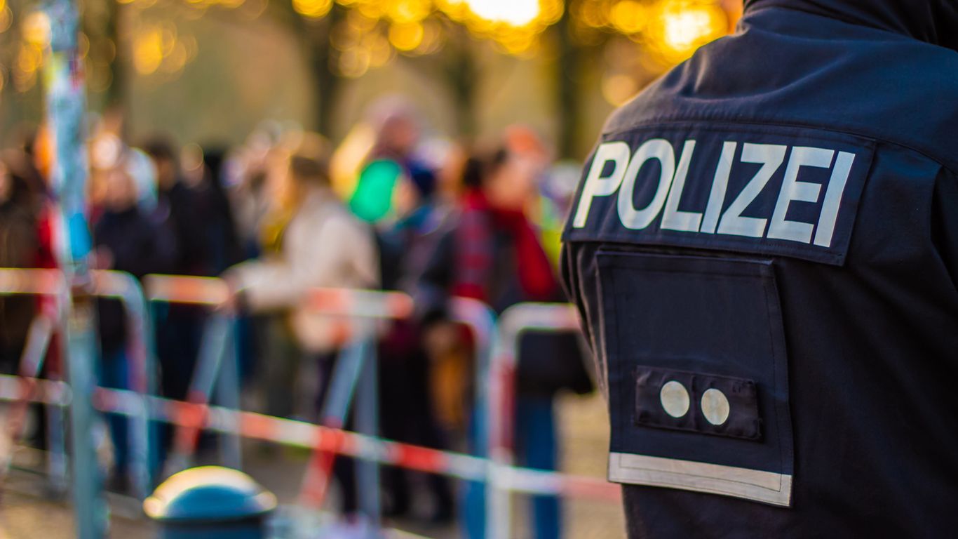 Police officer in foreground, people gathering in the background.