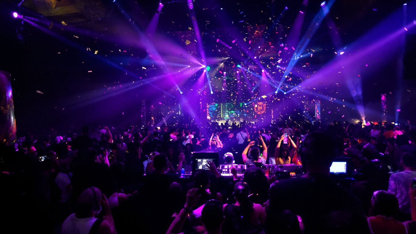 Tanzende Menschen vor DJ und bunten Lichtern im Club.